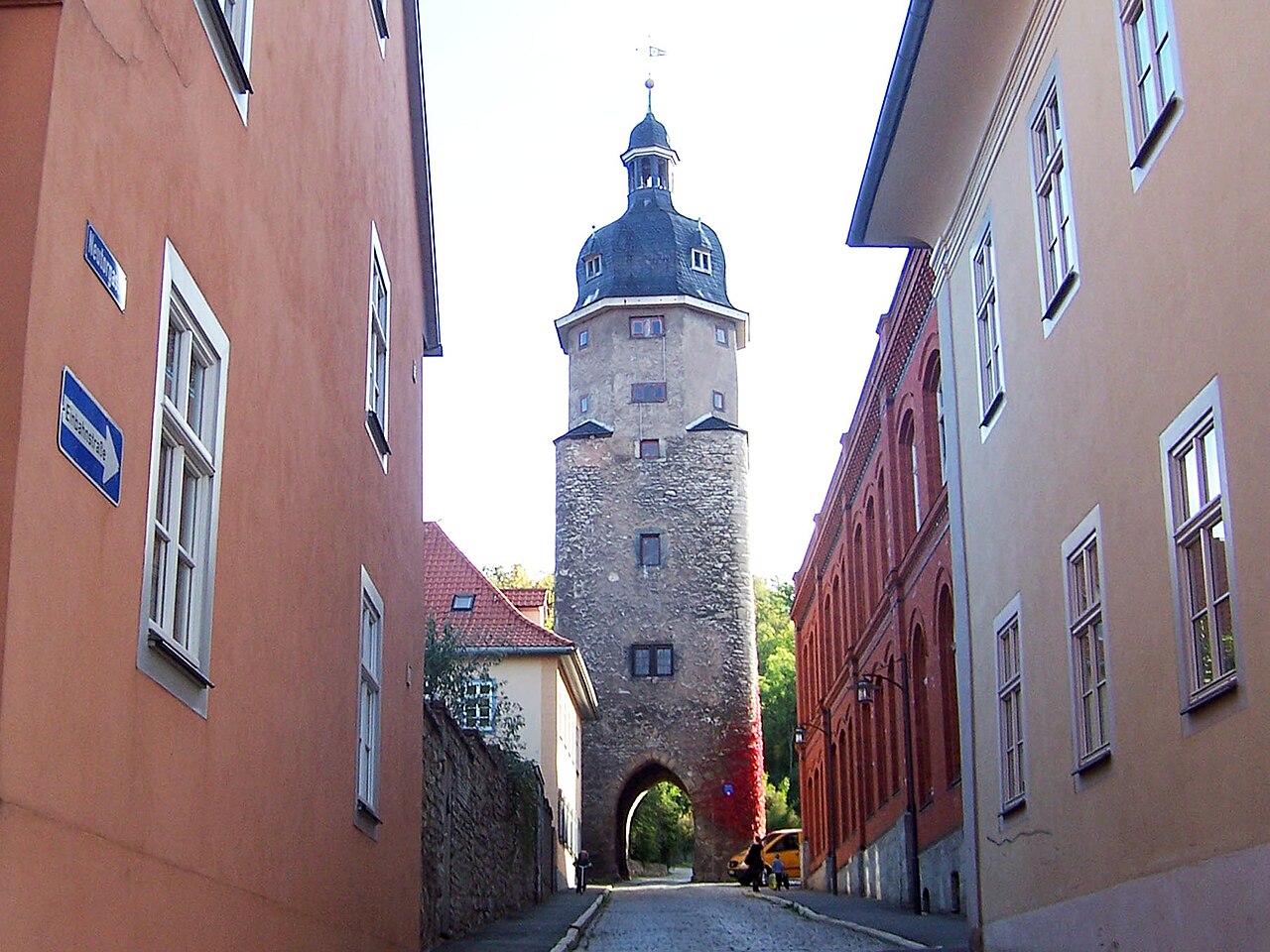 Torturm mit Durchfahrt und hoher Dachhaube am Ende einer Gasse.