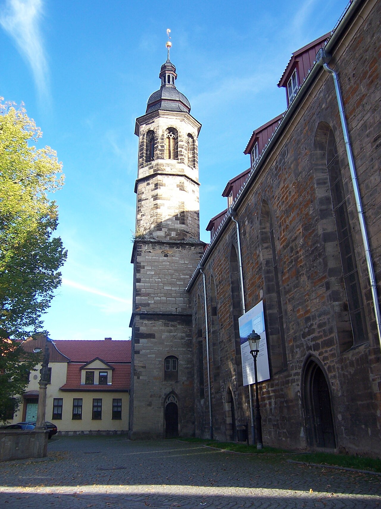 Hoher steinerner Glockenturm neben der Kirchenwand mit Spitzbogenfenstern.